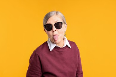 Photo of Senior woman in stylish outfit showing her tongue on orange background