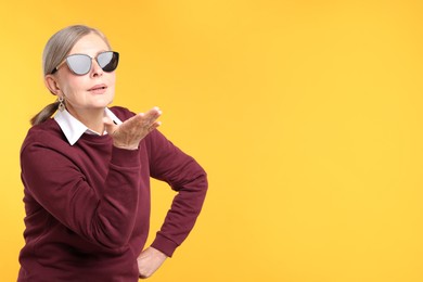 Photo of Senior woman in stylish outfit blowing kiss on orange background, space for text
