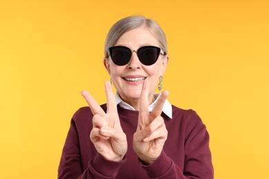 Photo of Happy senior woman in stylish outfit showing V-signs on orange background