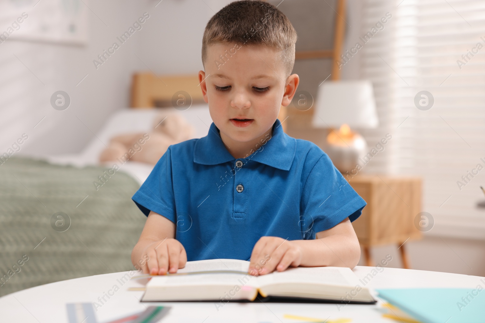 Photo of Dyslexia. Little boy reading book at table indoors