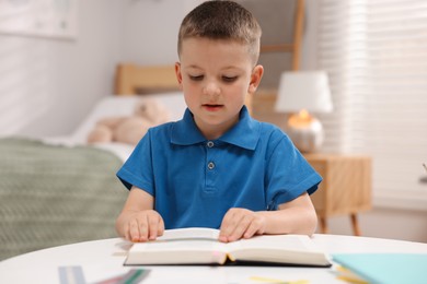 Photo of Dyslexia. Little boy reading book at table indoors