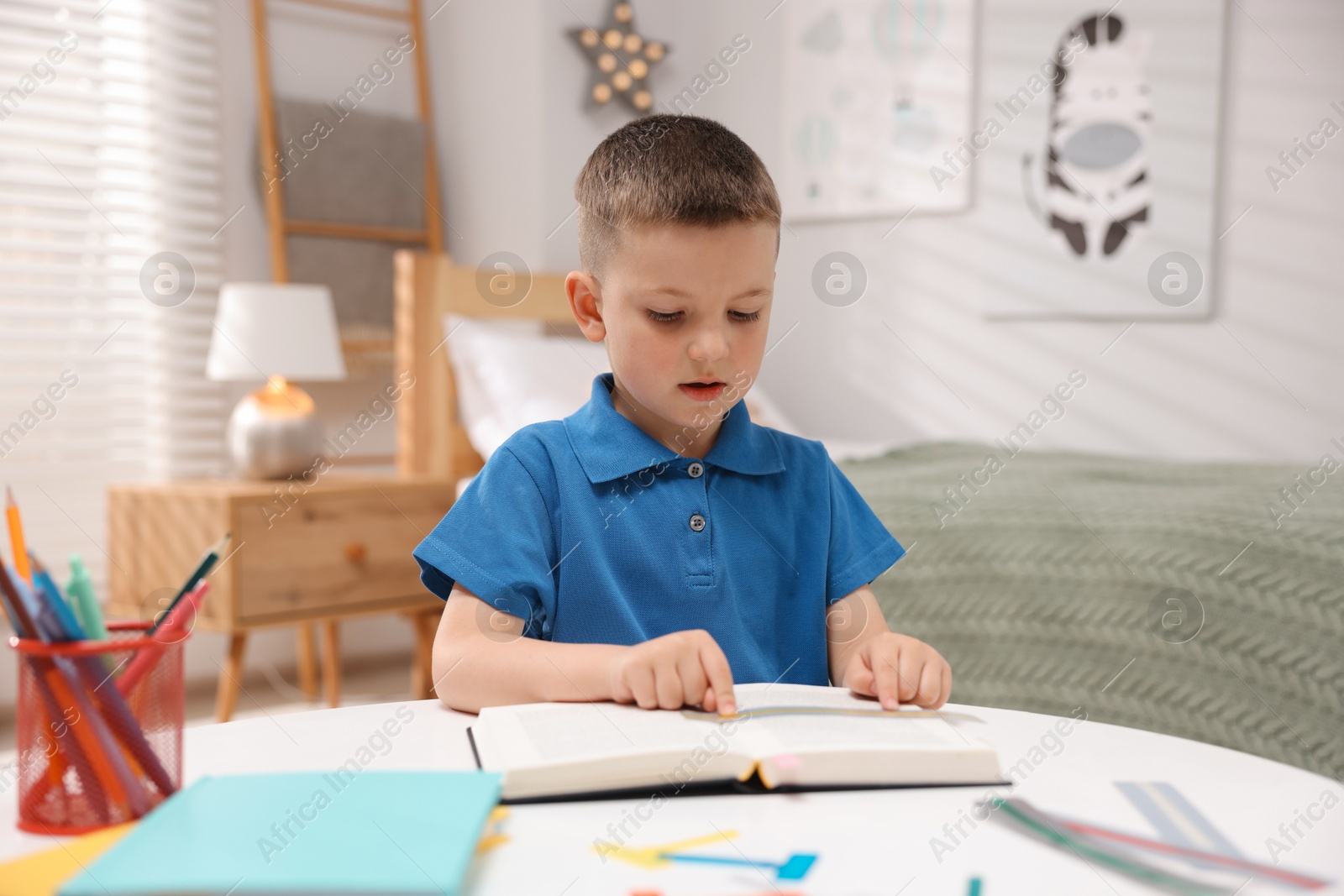 Photo of Dyslexia. Little boy reading book at table indoors