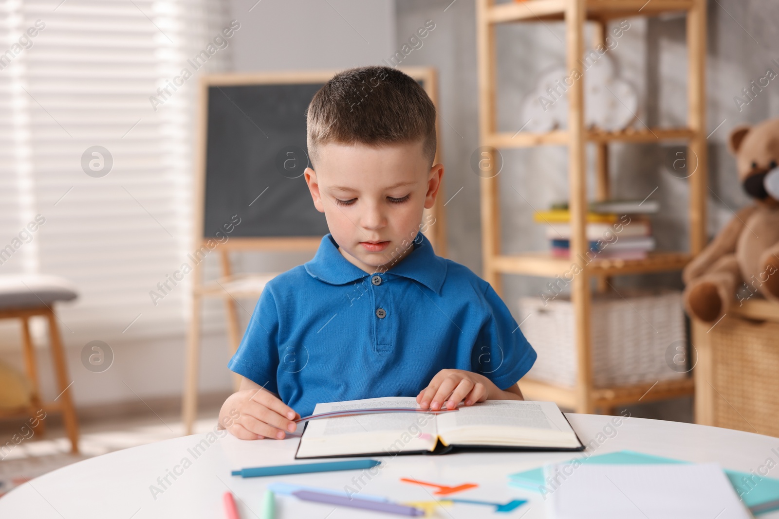 Photo of Dyslexia. Little boy reading book at table indoors