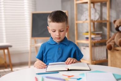 Photo of Dyslexia. Little boy reading book at table indoors