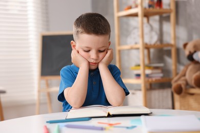 Photo of Dyslexia. Little boy reading book at table indoors