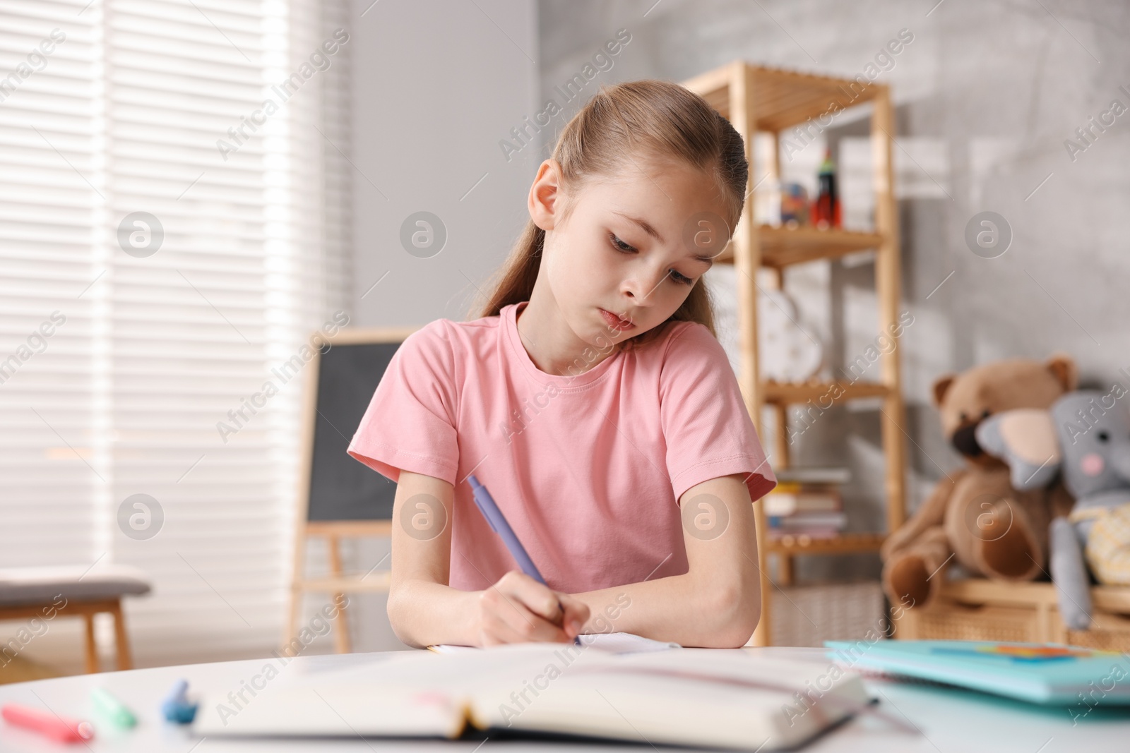 Photo of Dyslexia. Little girl writing at table indoors