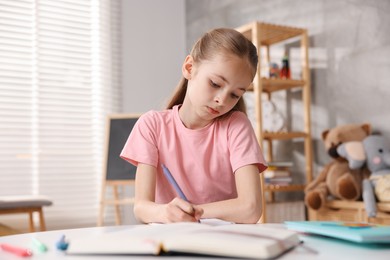Photo of Dyslexia. Little girl writing at table indoors