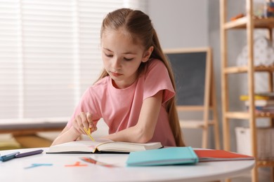 Photo of Dyslexia. Little girl reading book at table indoors