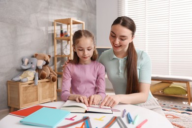 Photo of Dyslexia. Mother and her daughter reading book at table indoors