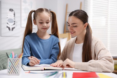 Photo of Dyslexia. Mother and her daughter reading book at table indoors