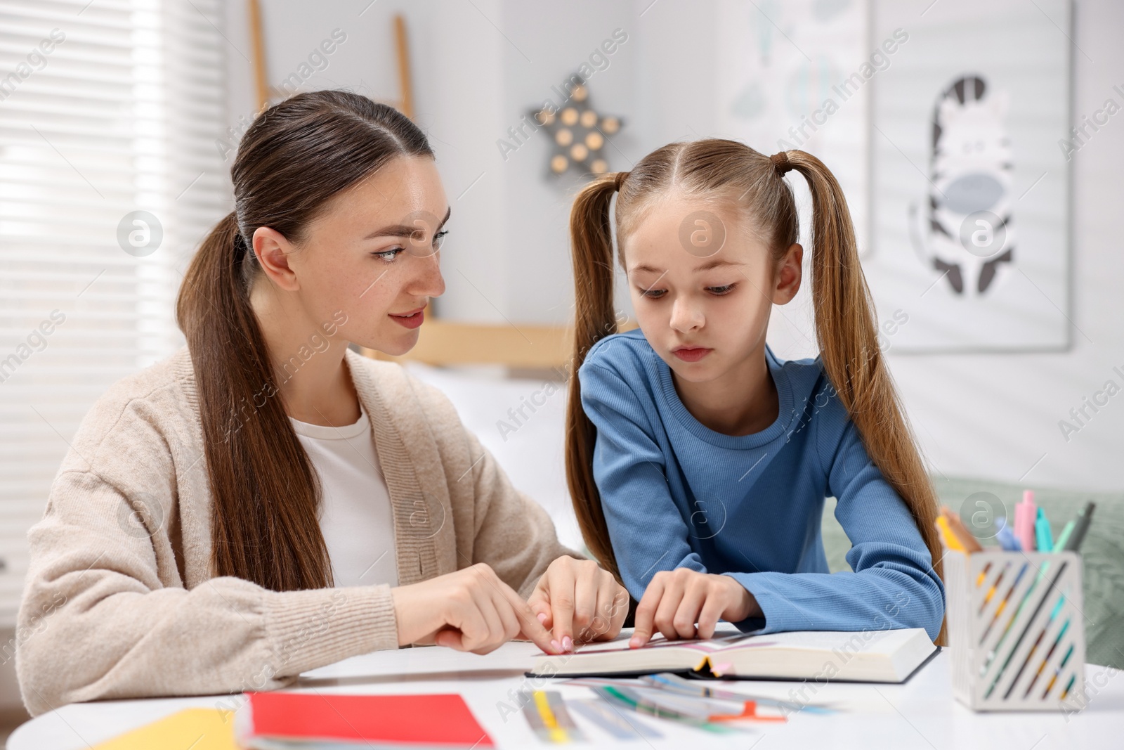 Dyslexia. Mother and her daughter reading book at table indoors Photo of Dyslexia. Mother and her daughter reading book at table indoors