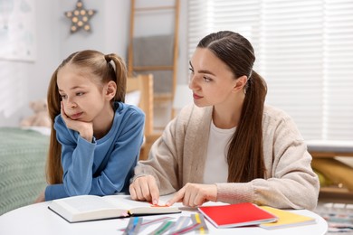 Photo of Dyslexia. Mother and her upset daughter reading book at table indoors