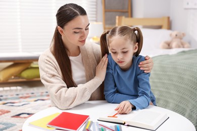 Photo of Dyslexia. Mother and her daughter reading book at table indoors