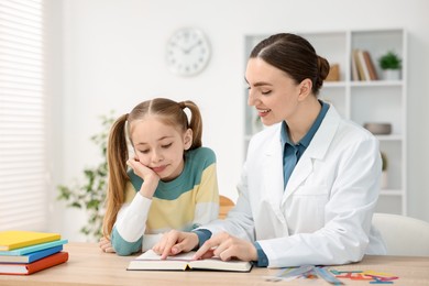 Photo of Dyslexia treatment. Pediatrician working with little girl at table indoors