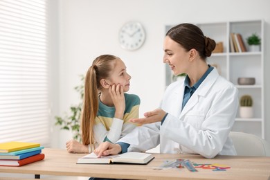Photo of Dyslexia treatment. Pediatrician working with little girl at table indoors