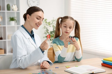 Photo of Dyslexia treatment. Pediatrician working with little girl at table indoors