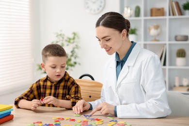 Photo of Dyslexia treatment. Pediatrician working with little boy at table indoors