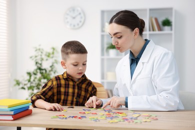 Photo of Dyslexia treatment. Pediatrician working with little boy at table indoors