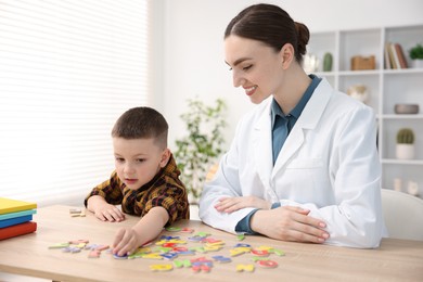 Photo of Dyslexia treatment. Pediatrician working with little boy at table indoors