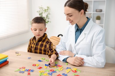 Photo of Dyslexia treatment. Pediatrician working with little boy at table indoors