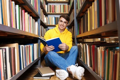 Photo of Man reading book near shelves in public library