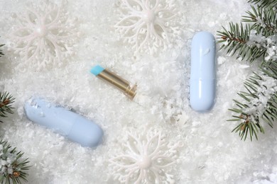 Photo of Moisturizing lip balms, Christmas decor and fir tree branches on artificial snow, flat lay. Winter care