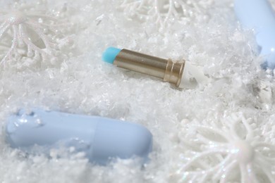 Photo of Moisturizing lip balms and Christmas decor on artificial snow, closeup. Winter care