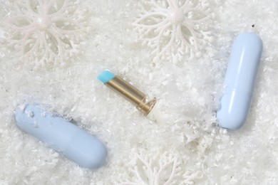 Photo of Moisturizing lip balms and Christmas decor on artificial snow, flat lay. Winter care