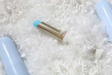 Photo of Moisturizing lip balms and Christmas decor on artificial snow, closeup. Winter care