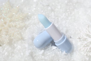 Photo of Moisturizing lip balm and Christmas decor on artificial snow, closeup. Winter care