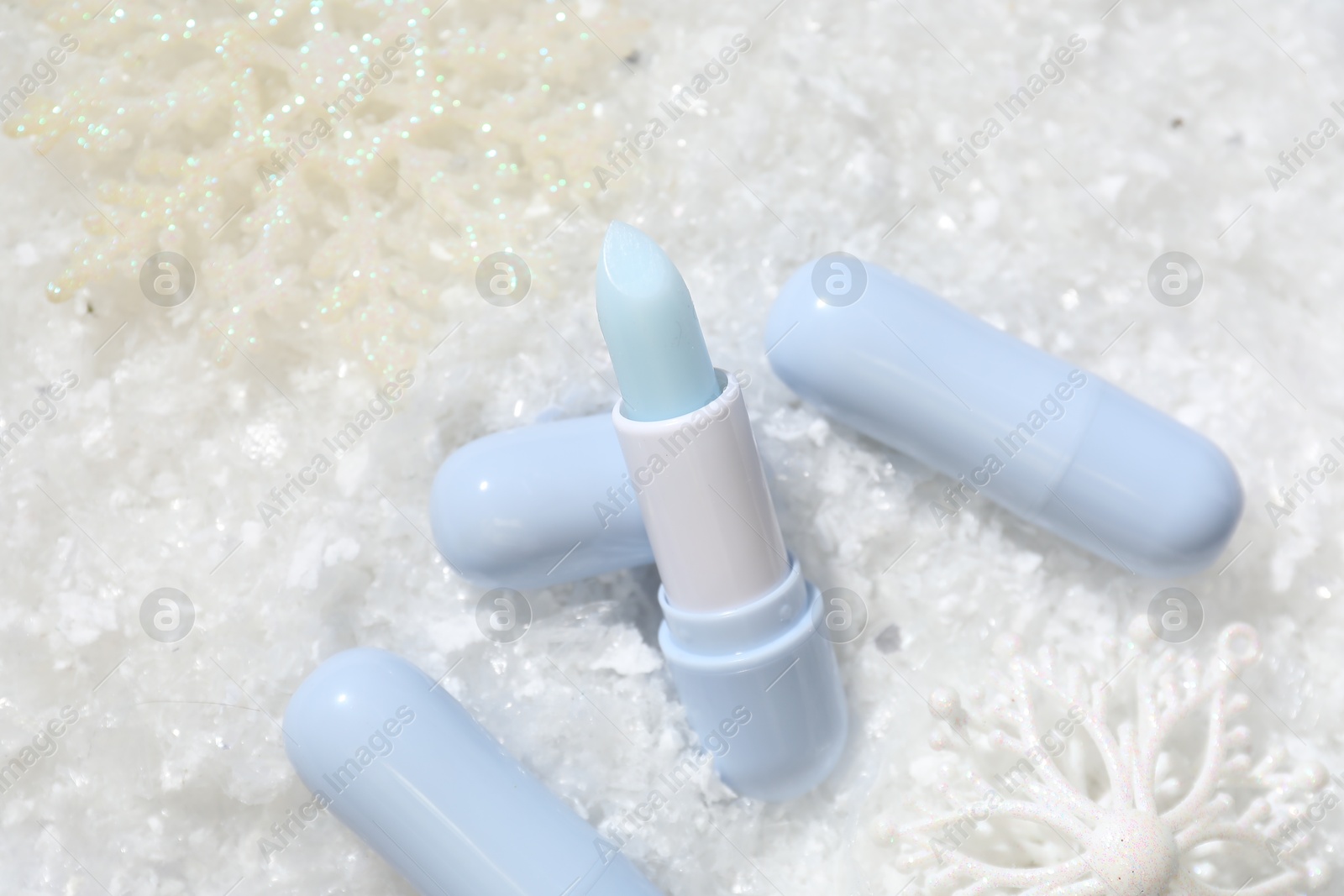 Moisturizing lip balms and Christmas decor on artificial snow, flat lay. Winter care Photo of Moisturizing lip balms and Christmas decor on artificial snow, flat lay. Winter care