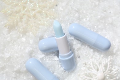Photo of Moisturizing lip balms and Christmas decor on artificial snow, flat lay. Winter care