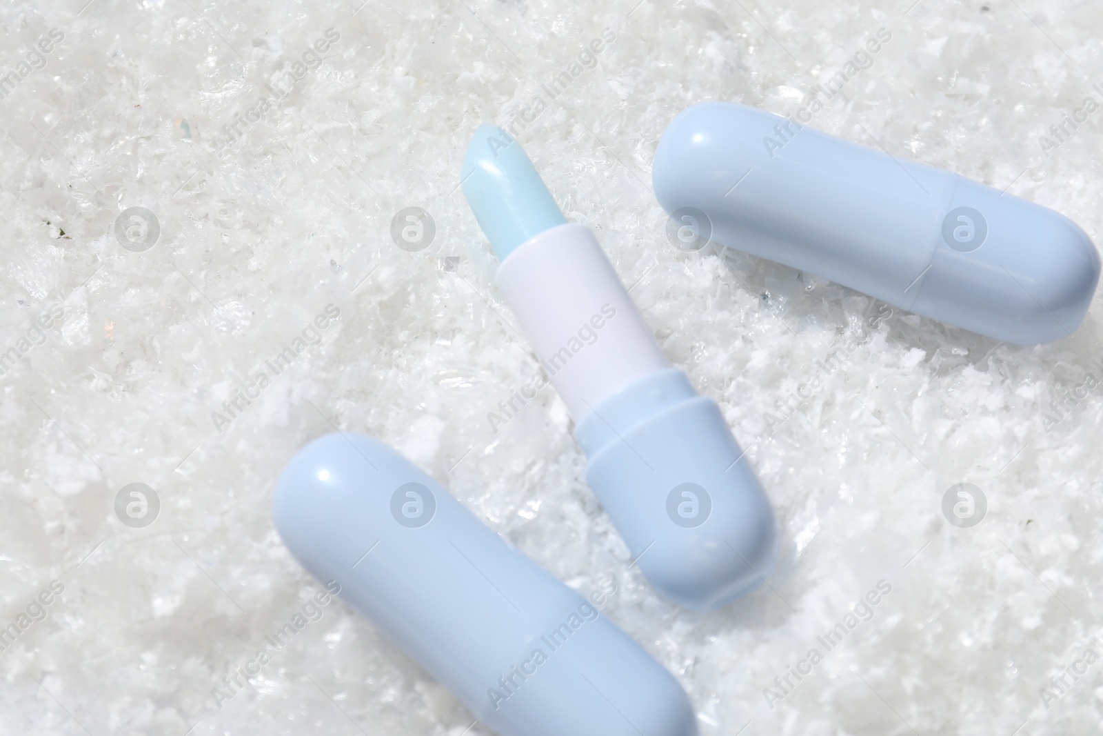 Photo of Moisturizing lip balms on artificial snow, flat lay. Space for text