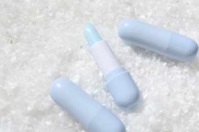 Photo of Moisturizing lip balms on artificial snow, flat lay. Space for text