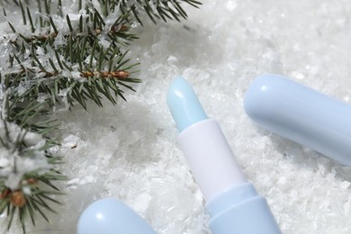 Photo of Moisturizing lip balms and fir tree branches on artificial snow, closeup. Winter care