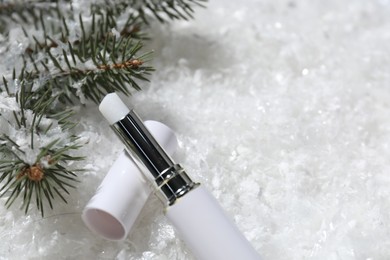 Photo of Moisturizing lip balm and fir tree branches on artificial snow, closeup. Space for text