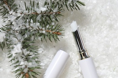 Photo of Moisturizing lip balm and fir tree branches on artificial snow, flat lay. Winter care