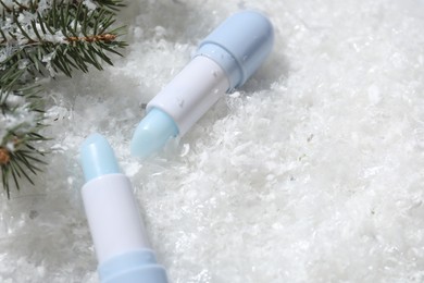 Photo of Moisturizing lip balms and fir tree branches on artificial snow, closeup. Space for text