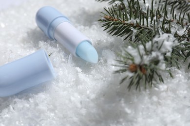 Photo of Moisturizing lip balm and fir tree branches on artificial snow, closeup. Winter care
