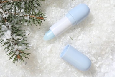 Photo of Moisturizing lip balm and fir tree branches on artificial snow, flat lay. Winter care