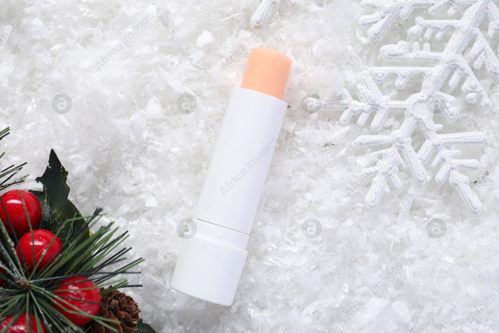 Photo of Moisturizing lip balm and Christmas decor on artificial snow, flat lay. Winter care