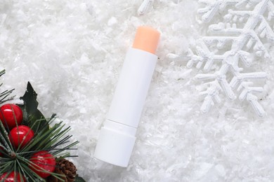 Photo of Moisturizing lip balm and Christmas decor on artificial snow, flat lay. Winter care