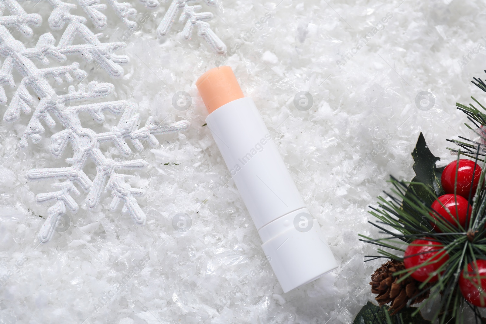 Photo of Moisturizing lip balm and Christmas decor on artificial snow, flat lay. Winter care
