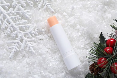 Photo of Moisturizing lip balm and Christmas decor on artificial snow, flat lay. Winter care