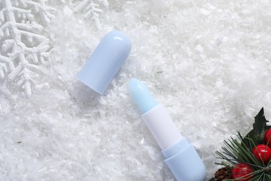 Photo of Moisturizing lip balm and Christmas decor on artificial snow, flat lay. Winter care
