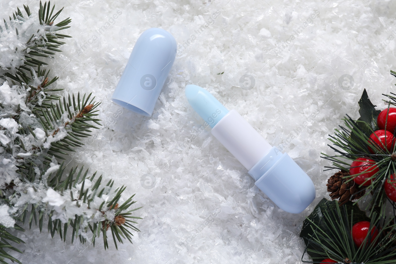 Photo of Moisturizing lip balm, Christmas decor and fir tree branches on artificial snow, flat lay. Winter care
