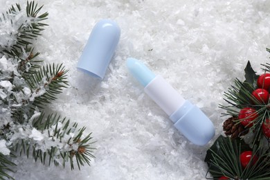 Photo of Moisturizing lip balm, Christmas decor and fir tree branches on artificial snow, flat lay. Winter care