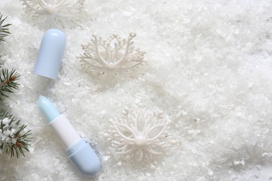 Photo of Moisturizing lip balm, Christmas decor and fir tree branches on artificial snow, flat lay. Space for text