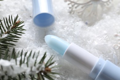 Photo of Moisturizing lip balm, Christmas decor and fir tree branches on artificial snow, closeup. Winter care