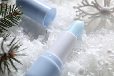 Photo of Moisturizing lip balm, Christmas decor and fir tree branches on artificial snow, closeup. Winter care